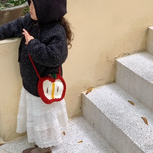 Handmade crochet apple shaped crossbody bag for kids shown in a warm outdoor setting
