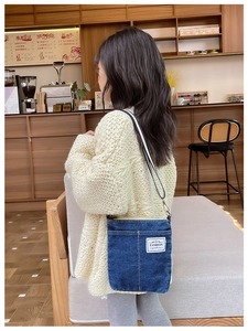 Detail of blue denim crossbody bag with FASHION label and striped strap in cafe setting