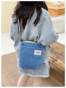 Detail of kids denim crossbody bag with fashion label and striped woven shoulder strap