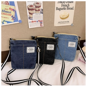 Detailed view of denim crossbody bag with fashion label and striped adjustable strap
