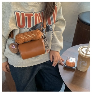 Detail of plush cylinder bag with bread texture and cute biscuit pendant charm
