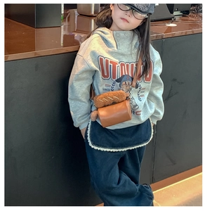Detail of kids brown leather cylinder bag featuring a cute plush bread charm and strap