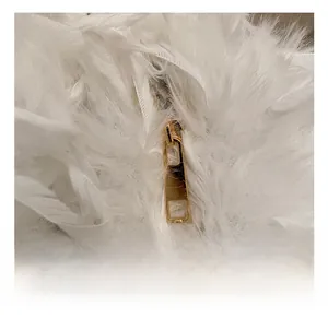 Détail du curseur de fermeture éclair doré poli sur un sac en fausse fourrure blanche