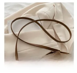 Detail of slim brown leather shoulder strap with gold metal buckle on girls bucket bag