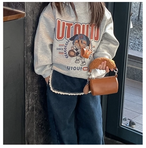 Detail of a brown plush cylinder handbag with fuzzy handles and a leather crossbody bag