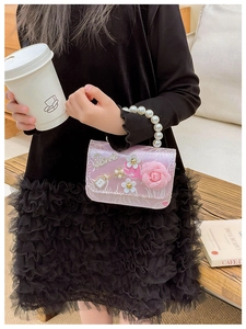 Detail of pink satin girl's bag with 3D roses, pearl handle, and rhinestone perfume patch