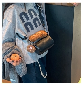 Detail of black faux leather mini cylinder bag with plush croissant and cookie charms