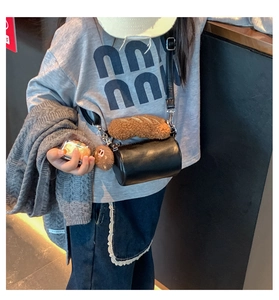 Detail of child's black cylinder crossbody bag featuring plush bread and biscuit charms