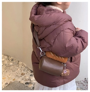 Detail of plush cylinder bag with cute cookie charm and leather finish on child model