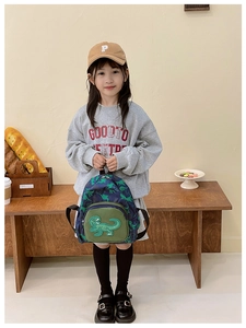 Dettaglio di simpatici dinosauri verdi su uno zainetto blu per bambini con tasche a zip