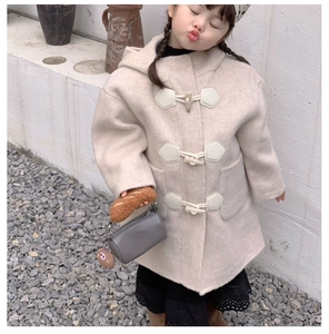 Detail of a grey cylindrical plush handbag with soft texture held by a girl in an elegant coat