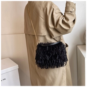 Detail of black crossbody bag with long feather fringes and gold chain strap on model