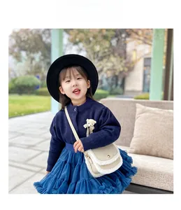 Girl in navy cardigan and tutu skirt wearing a beige plush trim crossbody bag outdoors