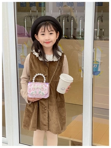 Close-up of pink satin children's bag with floral embroidery and pearl handle worn by model