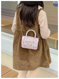 Detail of pink satin bag with rose embroidery, pearl handle, and gold chain strap