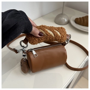 Detail of a brown cylinder crossbody bag with plush croissant handle and fuzzy charm