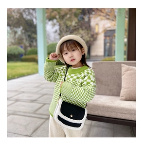 Detail of a kids' black and white crossbody bag with plush trim on a knit outfit
