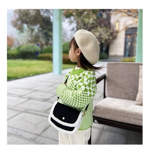 Kids black crossbody bag with white fur trim and gold button detail in outdoor scene