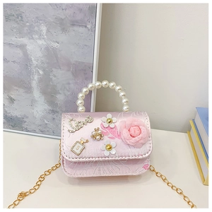 Close-up of pink satin mini bag with pearl handle, floral decor and gold chain details
