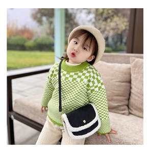 Close-up of stylish kids crossbody bag with plush trim paired with green checkered sweater