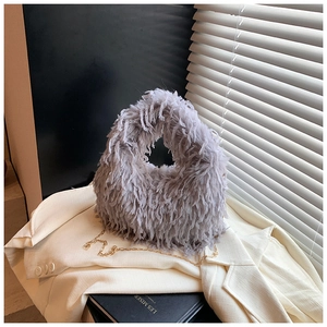 Détail du sac à main en fourrure grise avec anse ronde et chaîne dorée sur tissu blanc