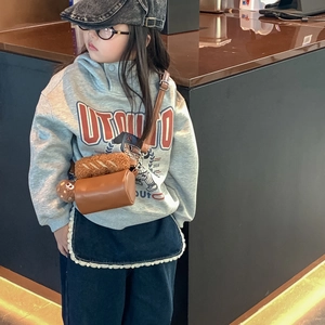 Chic brown cylinder crossbody bag for kids with cute plush bread charm on grey hoodie