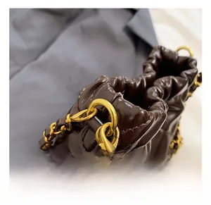 Detail einer dunkelbraunen Faltenledertasche mit goldenen Metallhaken und Kettenelementen