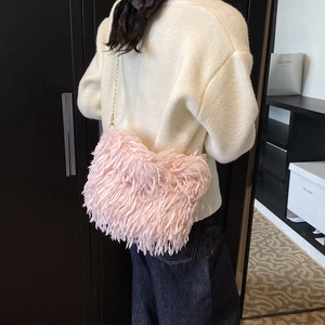 Sac bandoulière chic en fausse fourrure rose avec chaîne dorée porté par un mannequin