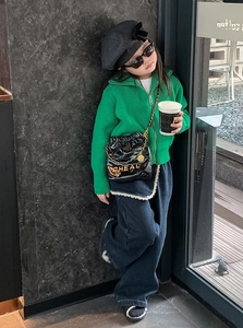 Detail eines grünen Kinder-Strickpullovers mit schwarzer Stepptasche und Goldkette