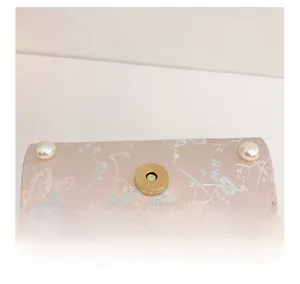Macro detail of floral silk fabric, golden metal magnetic clasp and pearl on pink bag