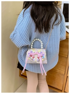 Pink embroidered kids handbag featuring floral patterns and a pearl handle on a model
