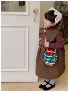 Detail of a child wearing a dark brown quilted dress with a green crochet Christmas tree bag