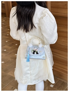 Detail of blue panda crossbody bag with pearl handle and silk tassel on child model