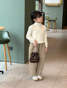 Detail eines Kindermodells mit brauner Stepp-Beuteltasche mit Kettenriemen und Goldlogo