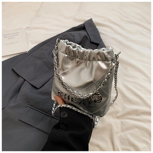 Details einer silbernen Stepptasche mit Metallbuchstaben, Kamelie und Kettenriemen