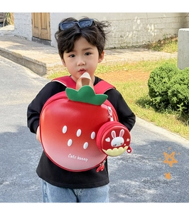 Detail of red strawberry kid backpack with green leaves and cute bunny charm on model