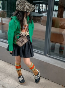 Detail of a kids stylish green knit cardigan paired with a checkered mini crossbody bag