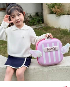 Pink hardshell child backpack with sequin wings and NMQI lettering in outdoor setting