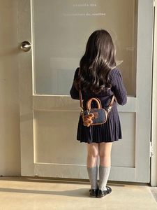 Rear view of child wearing a blue denim mini handbag with brown leather trim and bear charm