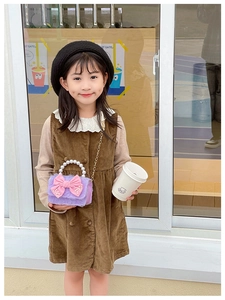 Girl in corduroy dress carrying a purple plush mini bag with pink bow and pearl handle