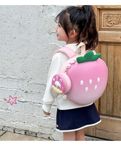 Pink strawberry kids backpack with cute bunny pouch worn by a child in an outdoor setting