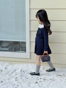 Detail of a dark blue knitted girl's dress with white ruffle collar and mini handbag