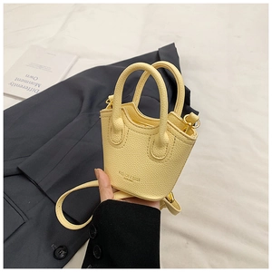 Detail of light yellow mini bucket bag featuring litchi grain texture and gold hardware