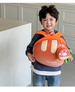 Detail view of a bright orange bunny children's hardshell backpack worn by a boy