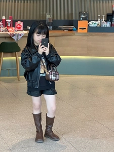 Toddler girl in biker jacket and boots showing a brown checkered crossbody small handbag