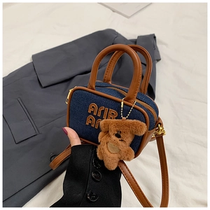 Detail view of denim handbag featuring brown leather handles and cute plush bear charm