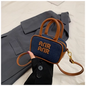 Detailed macro view of a mini denim crossbody bag with brown leather handles and AFIR embroidery