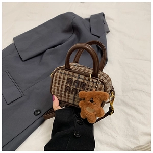 Detail of plaid mini bag with brown leather handle and cute plush bear charm accessory