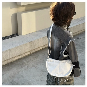 Close-up of white canvas crescent bag with adjustable strap in minimalist street style