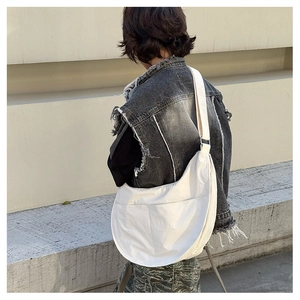 Street style view of cream canvas crescent bag with adjustable strap and front pocket
